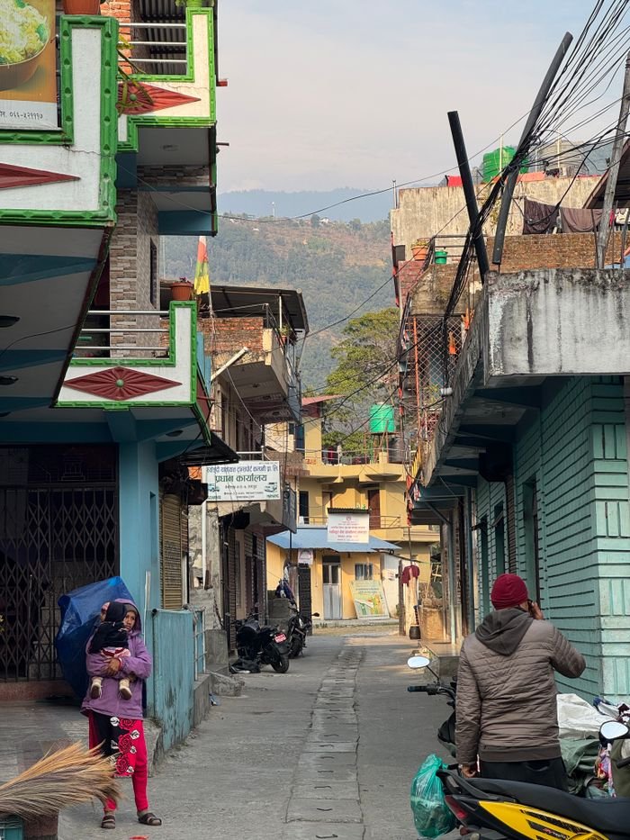 Vibrant street view of a Nepalese village with locals and colorful buildings under a clear sky.