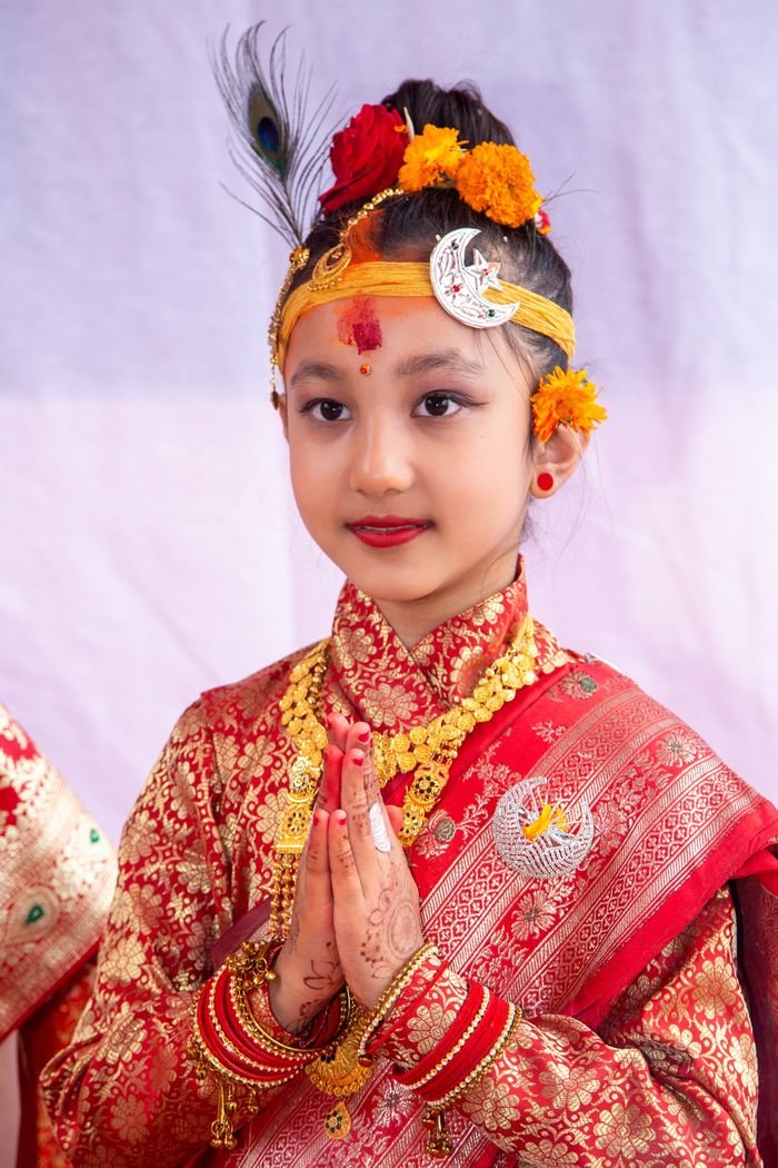 Young Nepali girl in vibrant traditional dress performing Namaste. Perfect for cultural and festive themes.